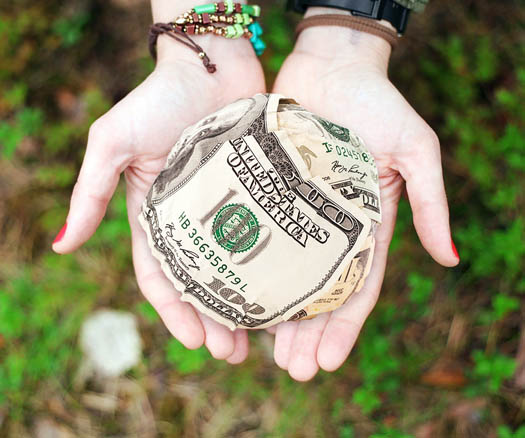 Outstretched hands holding a ball of $100 bills