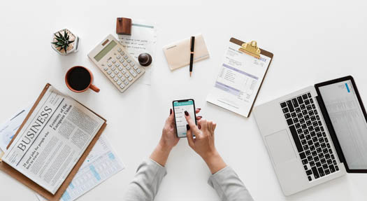 Woman holding phone with financial data on top of cluttered work desk