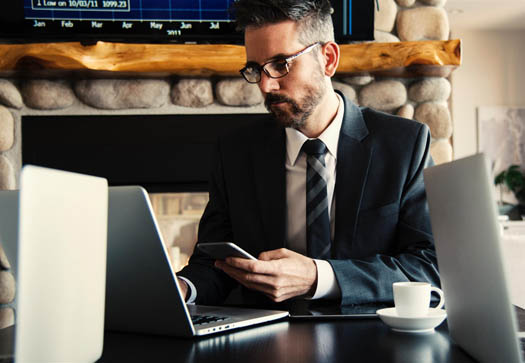 Man in suit looking at business data on laptop and cell phone screens