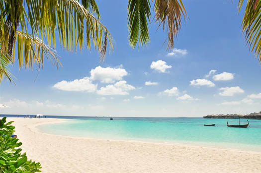 A white sand beach with two boats in the water off shore